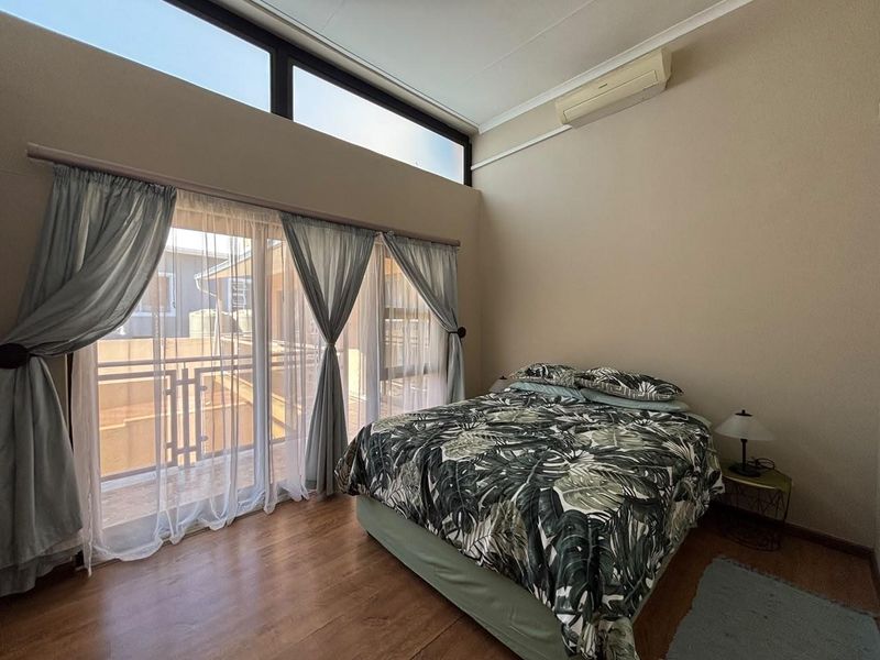 A bright bedroom featuring high ceilings with clerestory windows, laminate flooring, and direct access to a private balcony through sliding glass doors.