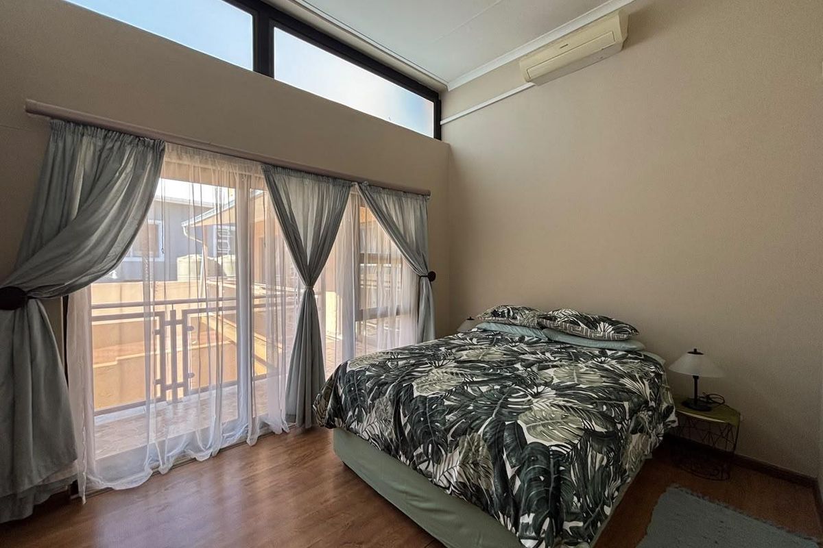 A bright bedroom featuring high ceilings with clerestory windows, laminate flooring, and direct access to a private balcony through sliding glass doors.