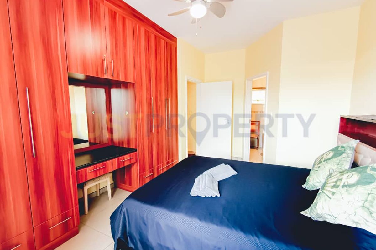 A bedroom featuring extensive floor-to-ceiling wood-finish built-in wardrobes with an integrated vanity station and a ceiling fan.
