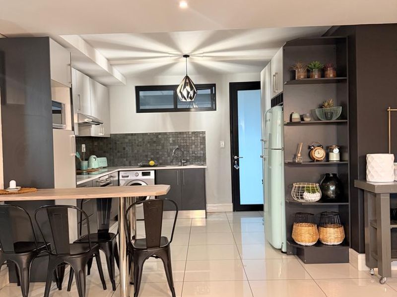 Modern kitchen featuring sleek dark cabinetry, tiled backsplash, integrated laundry facilities, and built-in shelving, finished with polished floor tiles and contemporary lighting.