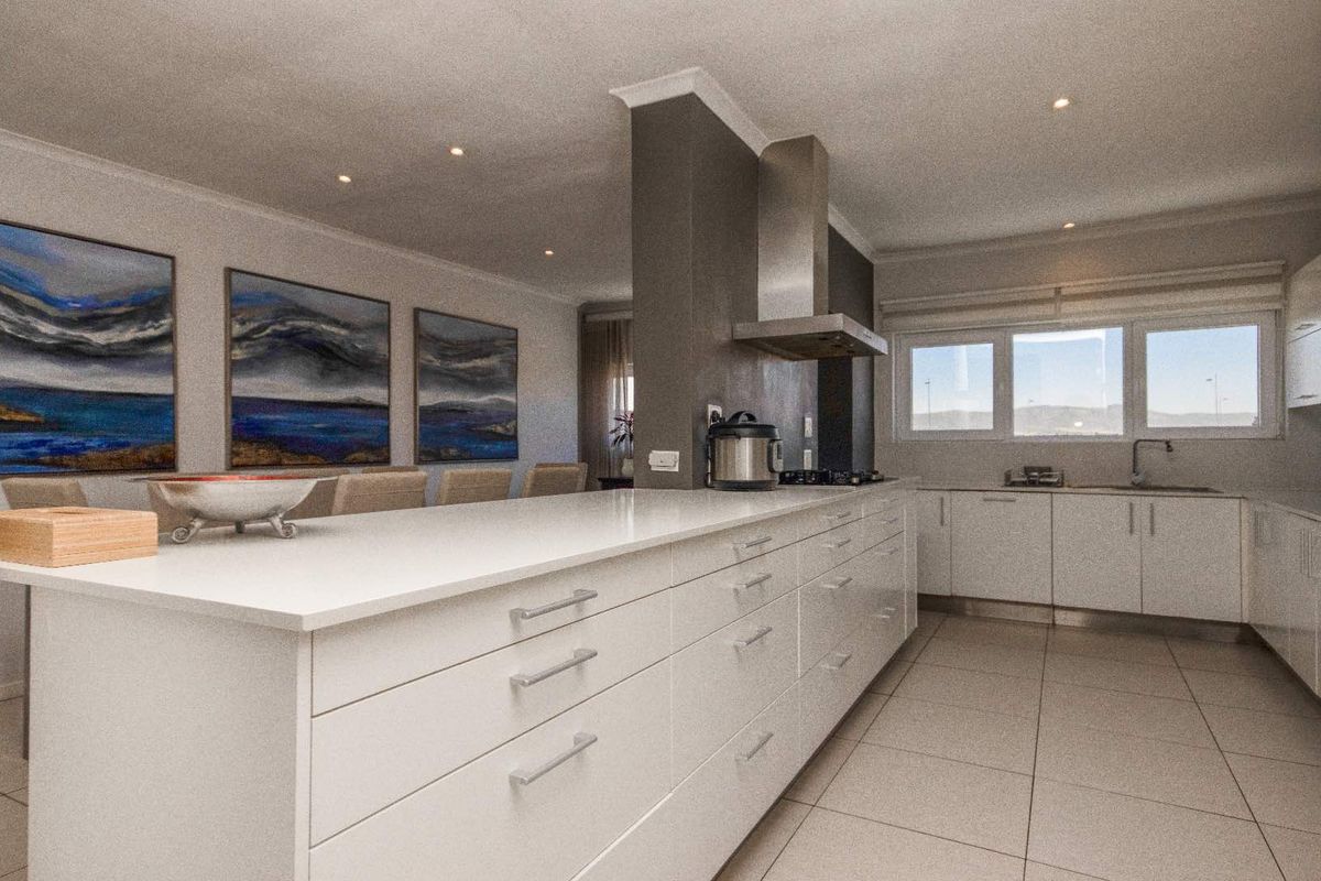 Modern kitchen featuring a large central island, sleek white cabinetry, stone countertops, and a stainless steel extractor fan with recessed lighting.