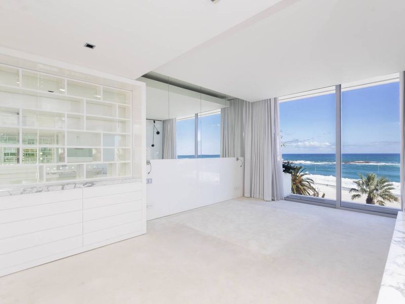 A bright, modern bedroom featuring built-in shelving, marble surfaces, and expansive floor-to-ceiling windows offering panoramic ocean views.