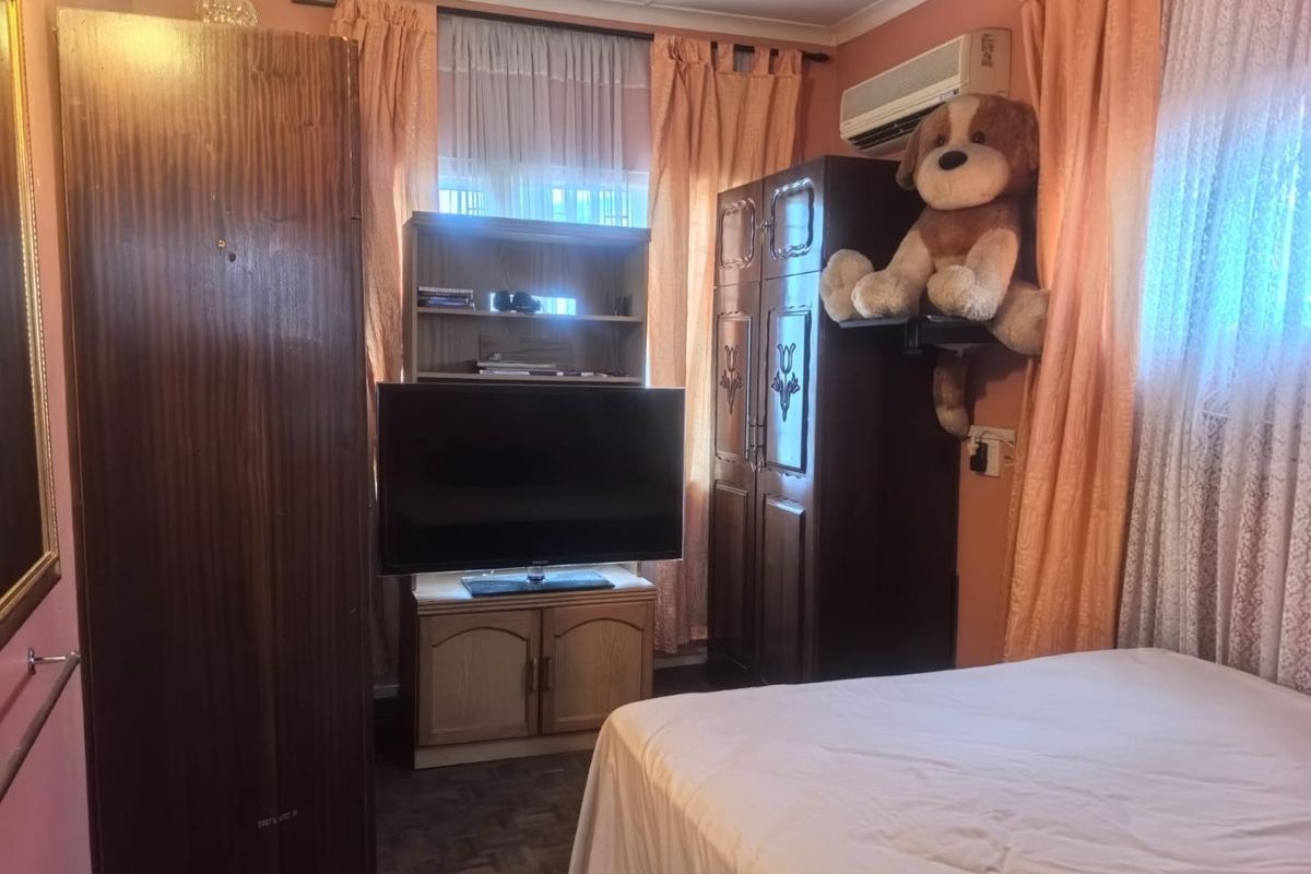 A bedroom featuring parquet flooring and a wall-mounted air conditioning unit, offering a functional space with traditional finishes.