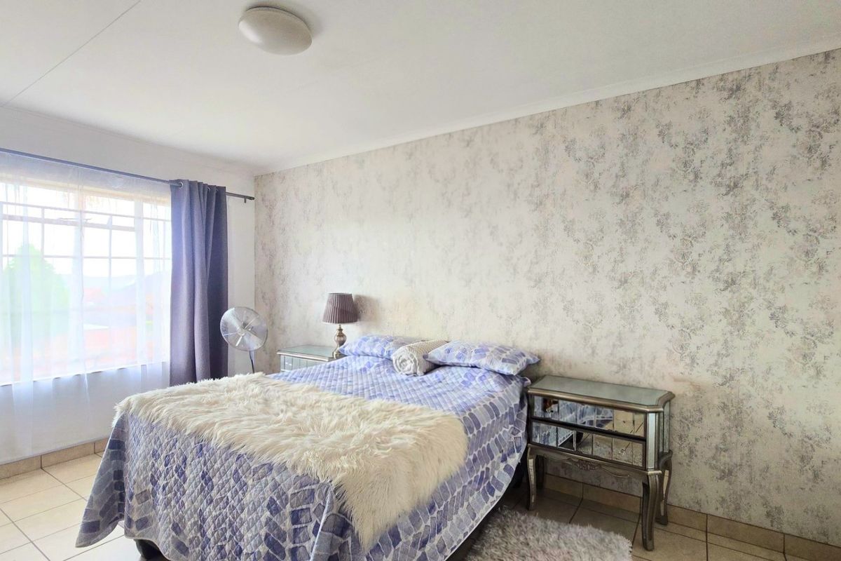 A bedroom featuring tiled flooring, a built-in cupboard, and a decorative wallpaper feature wall.