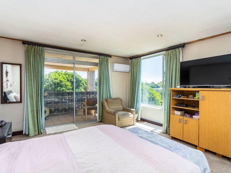 Spacious bedroom featuring large windows, a sliding glass door leading to a balcony, and a wall-mounted split-system air conditioner.