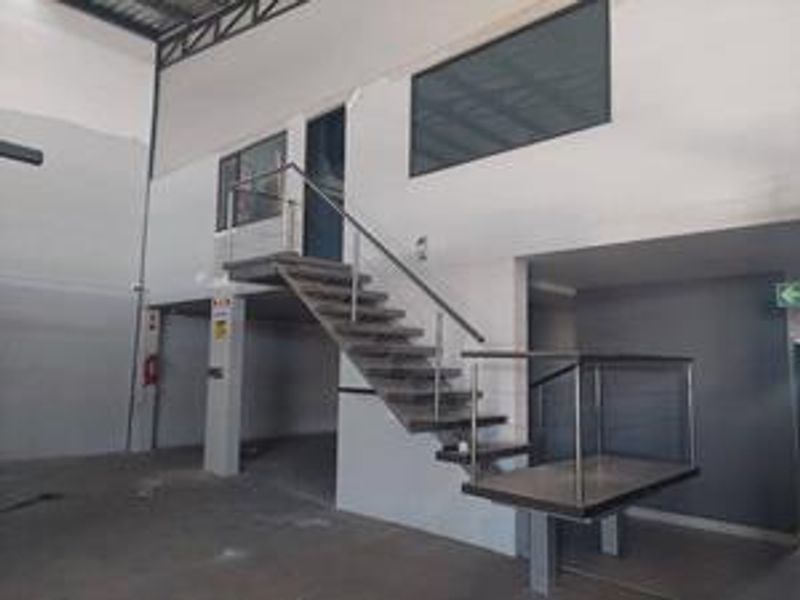 Industrial warehouse space featuring a mezzanine level with a modern metal staircase, stainless steel balustrades, and exposed structural steel elements.