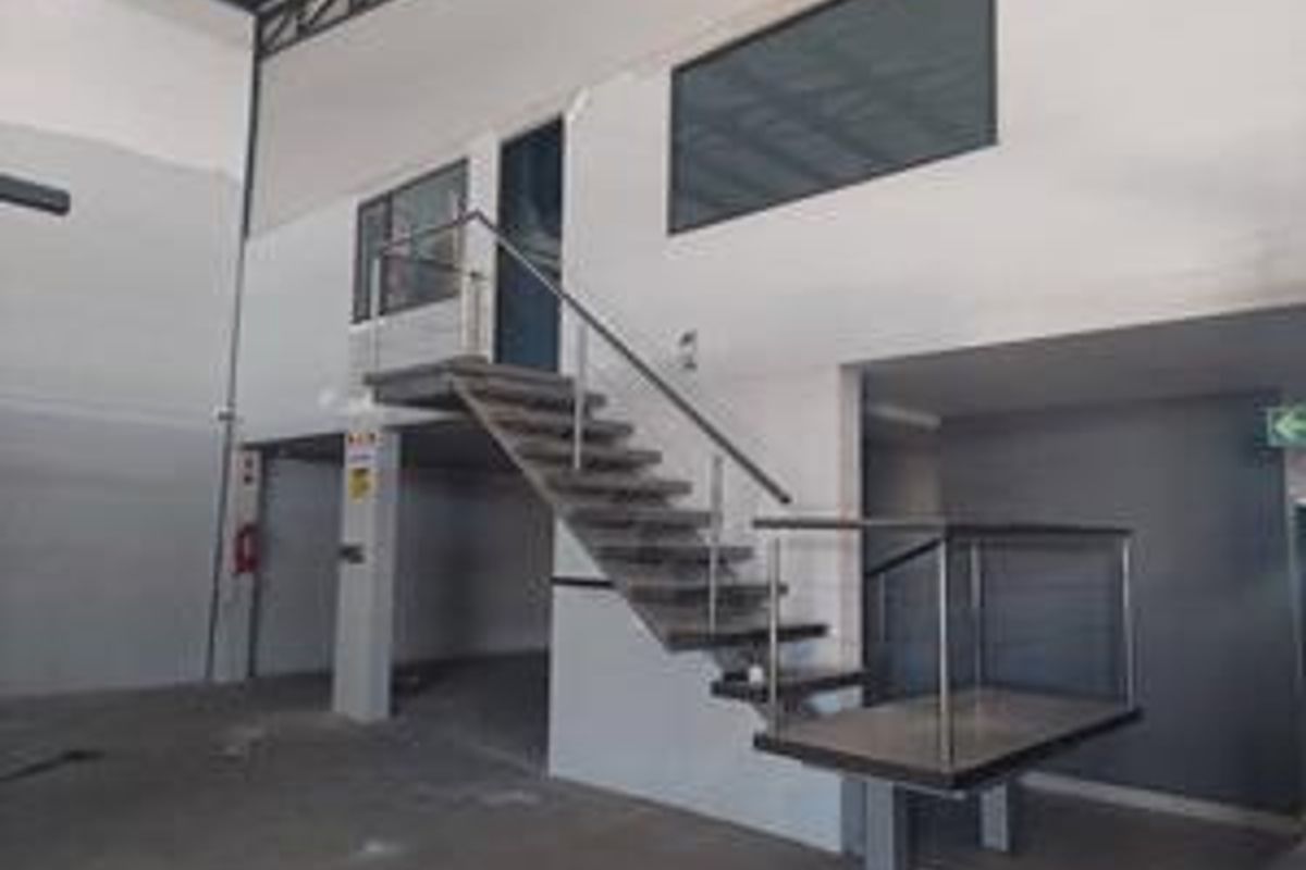 Industrial warehouse space featuring a mezzanine level with a modern metal staircase, stainless steel balustrades, and exposed structural steel elements.