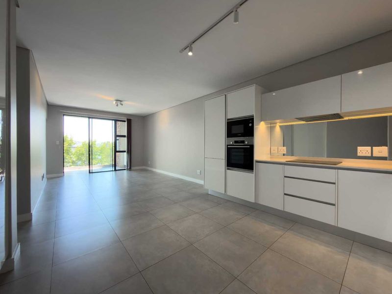 Modern open-plan living area featuring a sleek kitchen with built-in appliances, tiled flooring, and large sliding doors leading to an outdoor space.