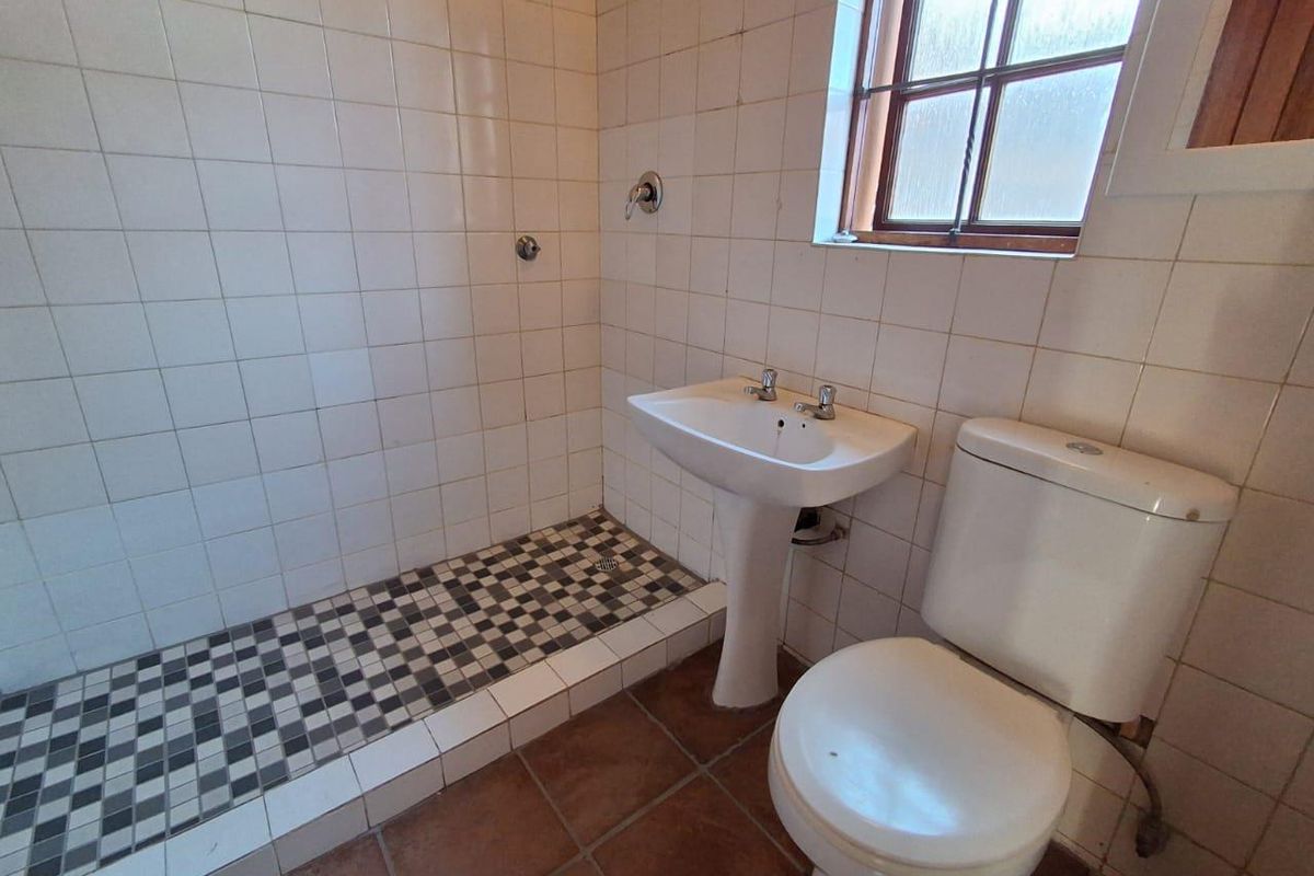 A functional bathroom featuring a walk-in shower with mosaic floor tiles, a pedestal washbasin, and a standard toilet with neutral wall tiling.