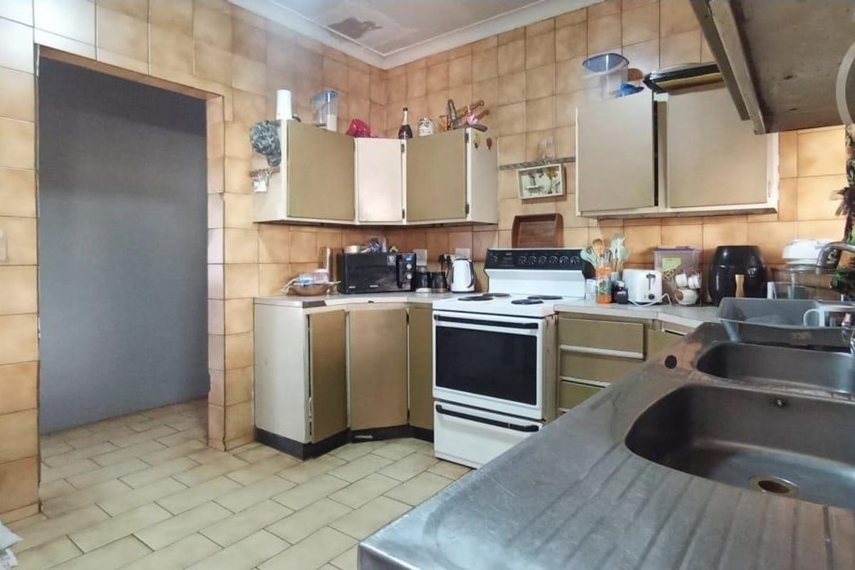 A dated kitchen featuring original cabinetry, tiled walls, and a stainless steel double sink, offering potential for a modern renovation.
