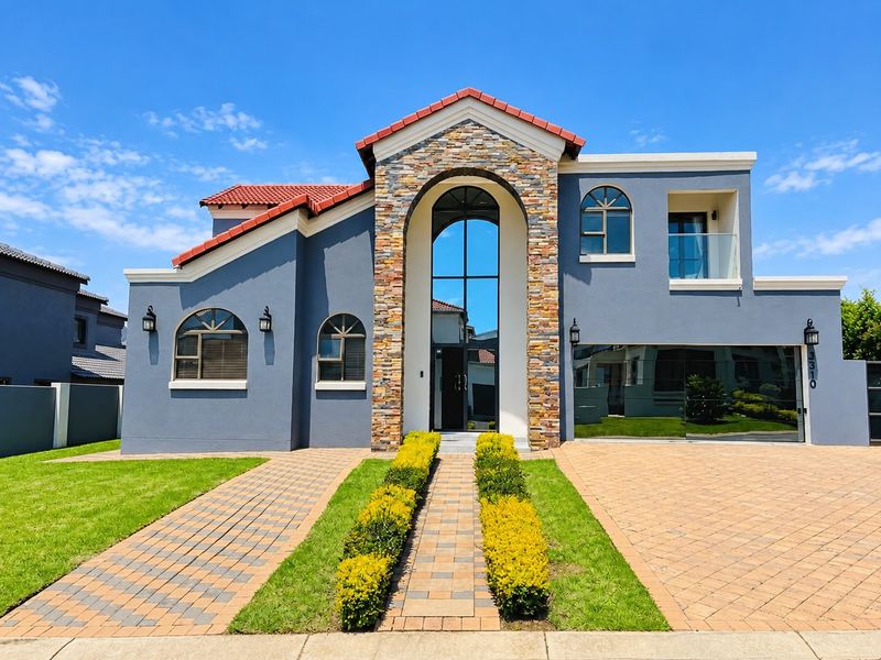 A modern double-story residence featuring stone cladding, a prominent arched entrance, tiled roof, and a paved driveway with an integrated double garage.