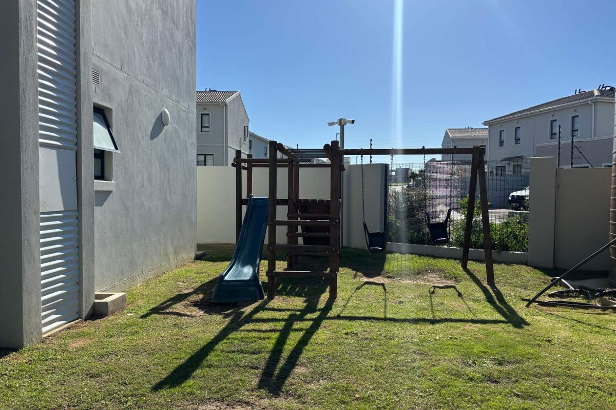 A private rear garden area featuring a lawn and a built-in wooden jungle gym with a slide and swings.