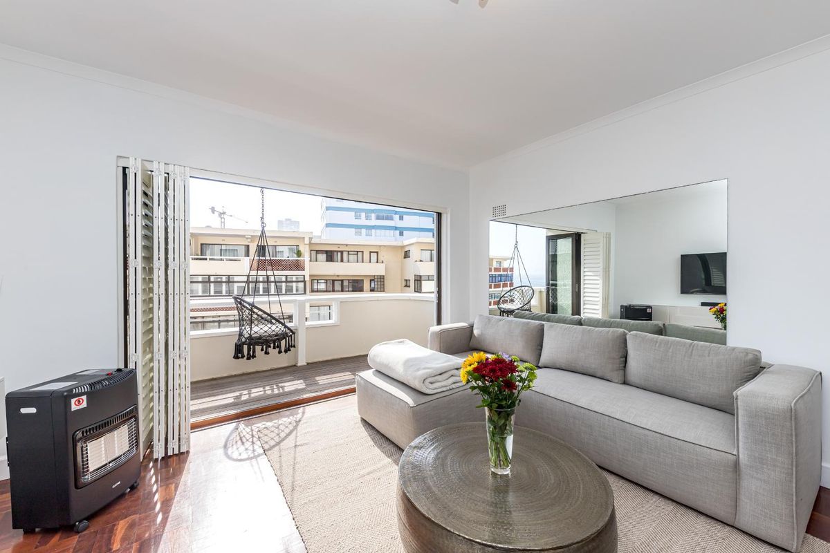 Bright living room featuring hardwood flooring, a large wall mirror, and seamless access to an outdoor balcony through bi-fold doors.