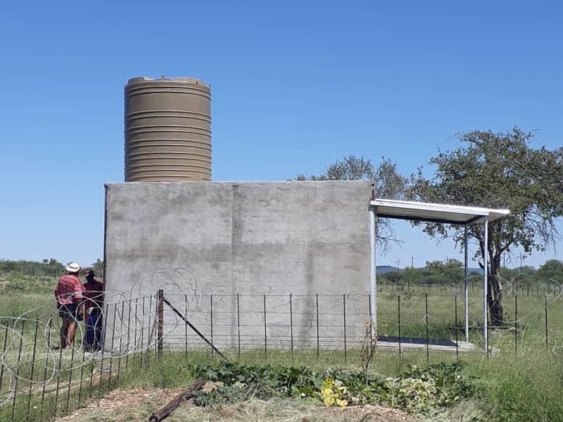 A functional utility structure featuring a large water storage tank mounted on a concrete base with an attached metal roof canopy.