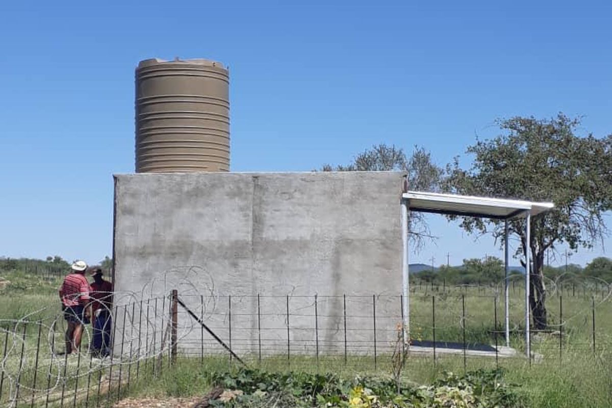 A functional utility structure featuring a large water storage tank mounted on a concrete base with an attached metal roof canopy.