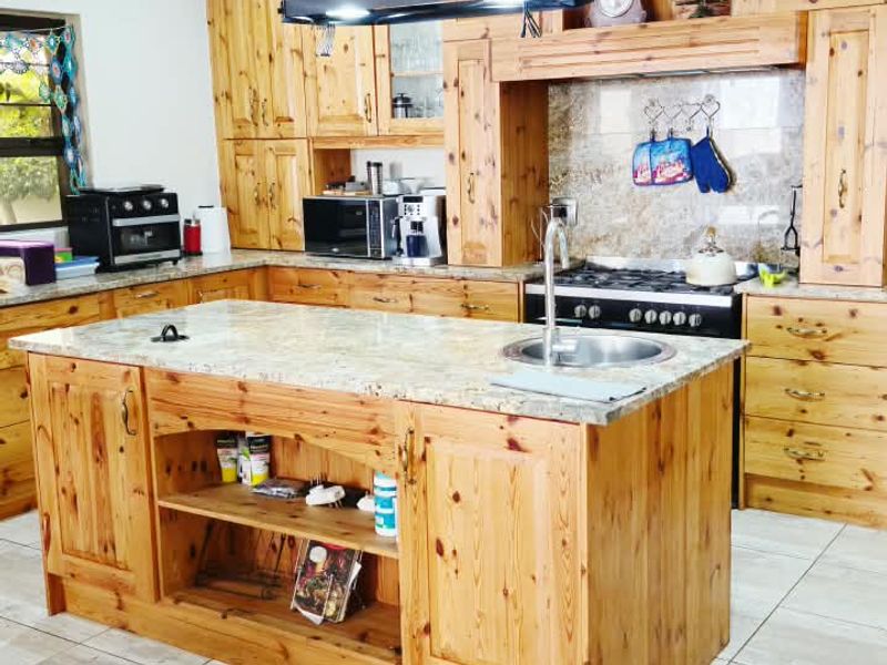 Spacious kitchen featuring extensive wooden cabinetry, a central island with granite countertops, a built-in gas hob, and tiled flooring throughout.