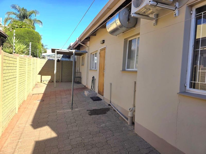 Rear exterior view of the townhouse featuring a paved courtyard, boundary wall, and external utility installations including a geyser and air conditioning unit.