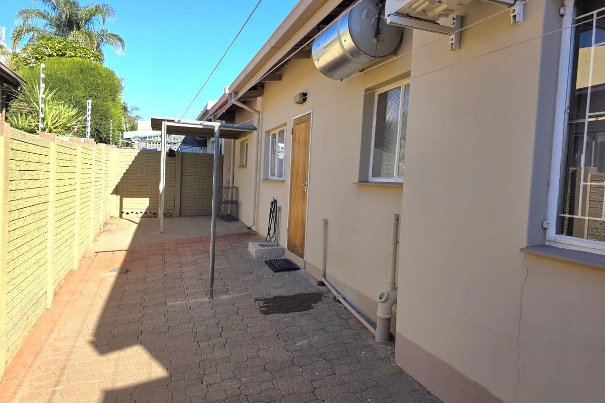 Rear exterior view of the townhouse featuring a paved courtyard, boundary wall, and external utility installations including a geyser and air conditioning unit.
