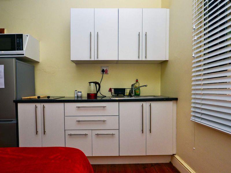 Compact kitchenette featuring white cabinetry, dark laminate countertops, a stainless steel sink, and venetian blinds for natural light control.