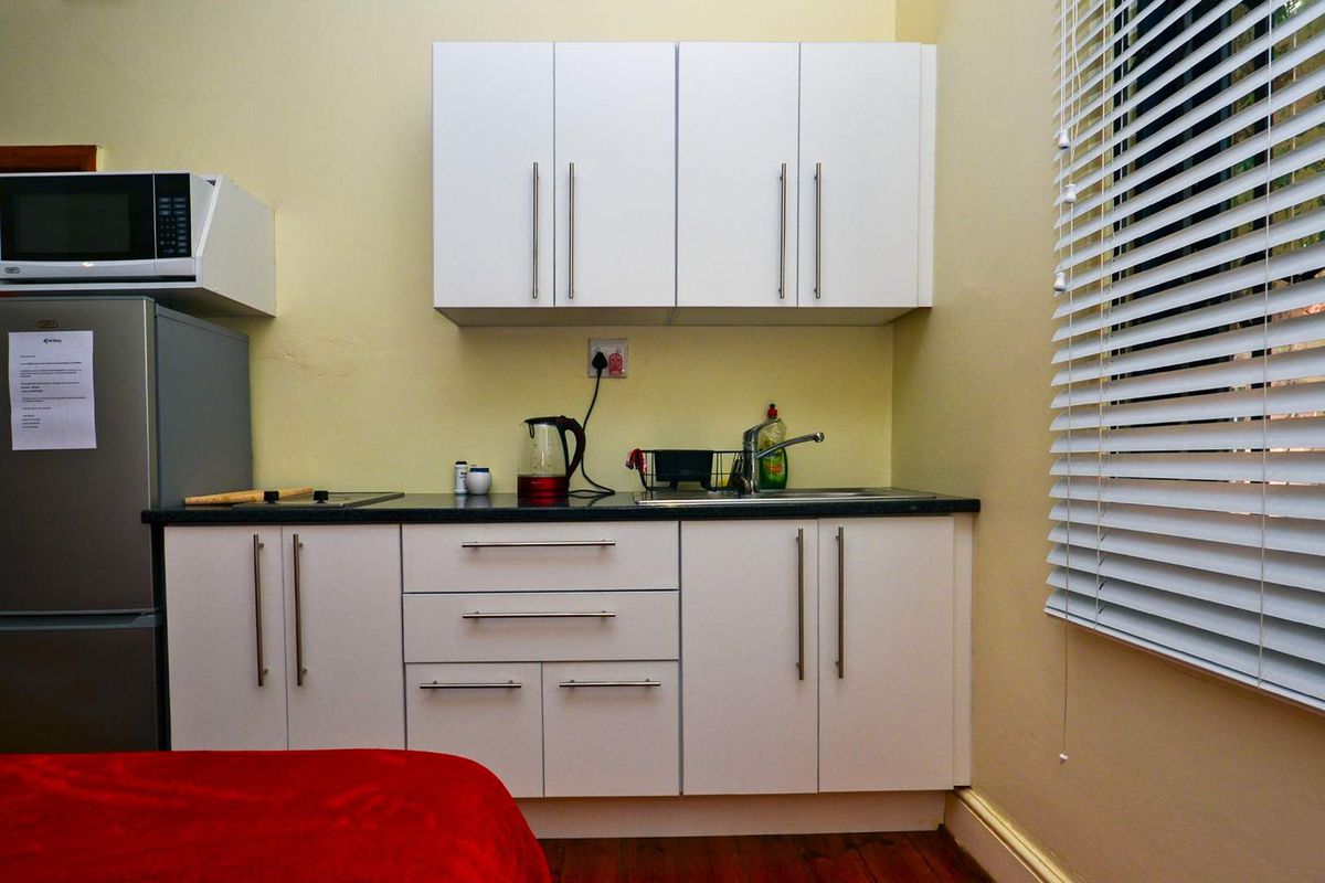Compact kitchenette featuring white cabinetry, dark laminate countertops, a stainless steel sink, and venetian blinds for natural light control.