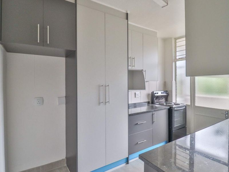 A clean, modern kitchen featuring neutral-toned built-in cabinetry, stone countertops, and a freestanding stove, offering a functional and well-maintained cooking space.
