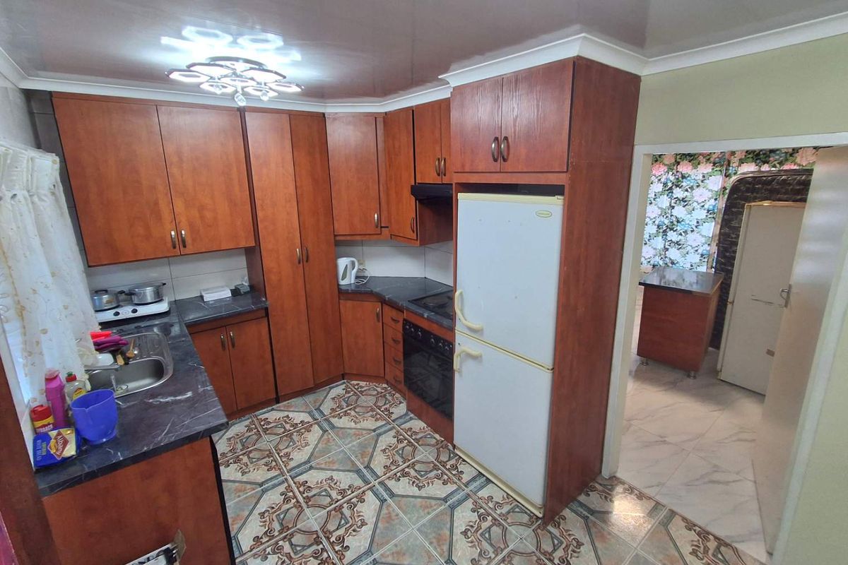 A functional kitchen featuring wood-finish cabinetry, dark laminate countertops, a built-in oven and hob, and patterned floor tiles.