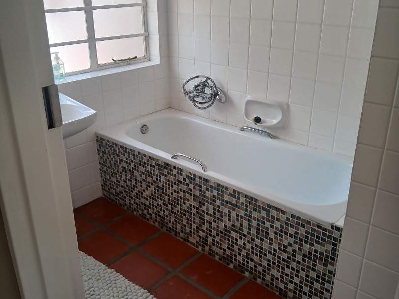 A functional bathroom featuring a built-in bathtub with a mosaic tile finish, wall-mounted basin, and terracotta floor tiles.