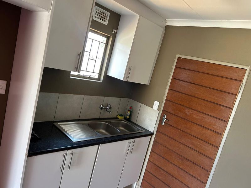 A functional kitchen area featuring white built-in cabinetry, a stainless steel double sink, tiled splashback, and a secure window.