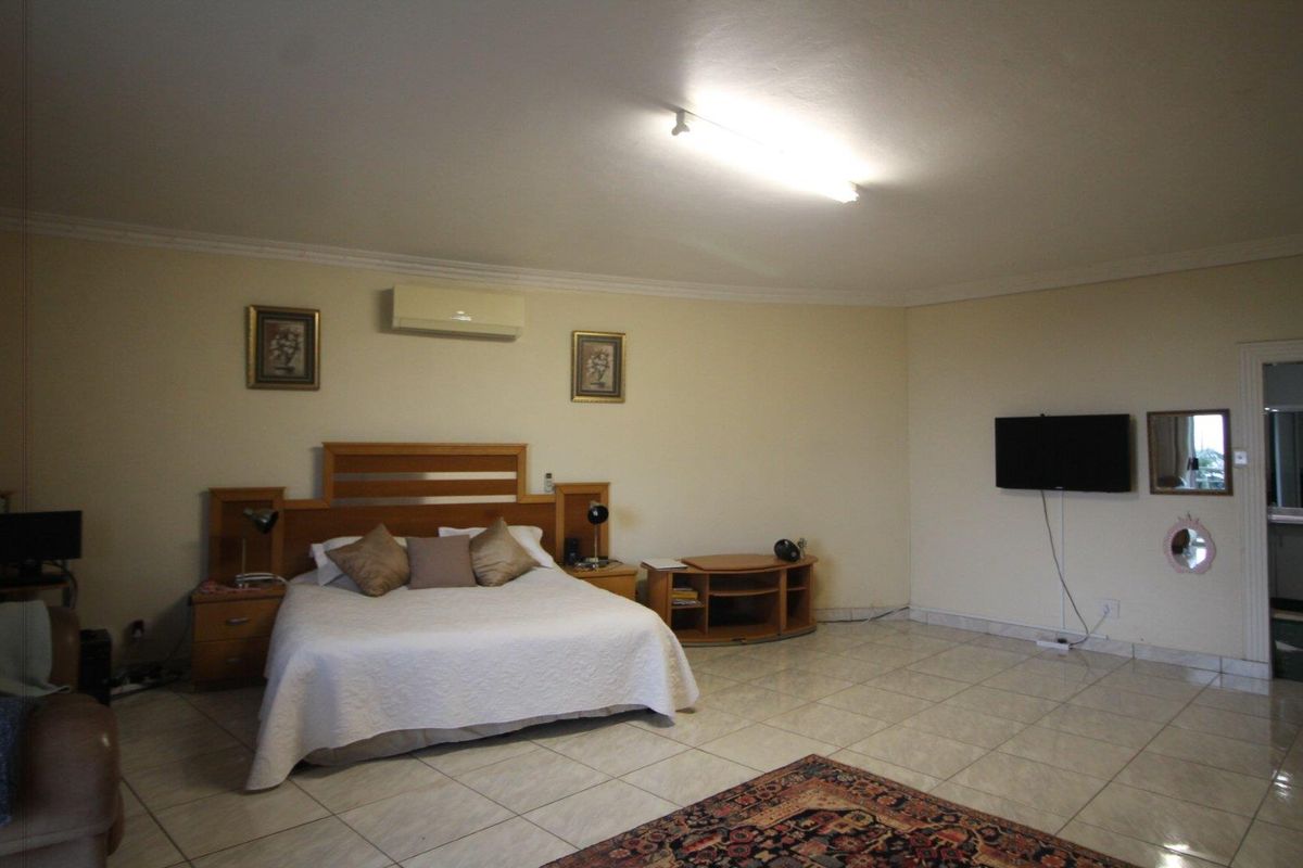 Spacious bedroom featuring tiled flooring, a wall-mounted air conditioning unit, and built-in headboard cabinetry.