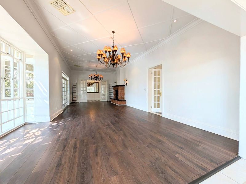 Spacious living room featuring dark laminate flooring, a classic fireplace, elegant coffered ceilings, and large windows providing ample natural light.