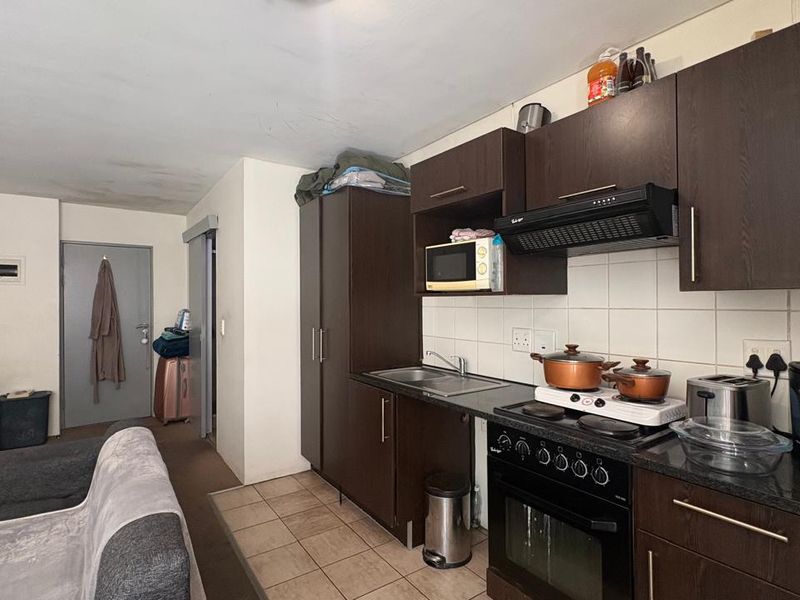 Open-plan apartment living area featuring a compact kitchen with dark wood cabinetry, built-in oven, and tiled flooring.