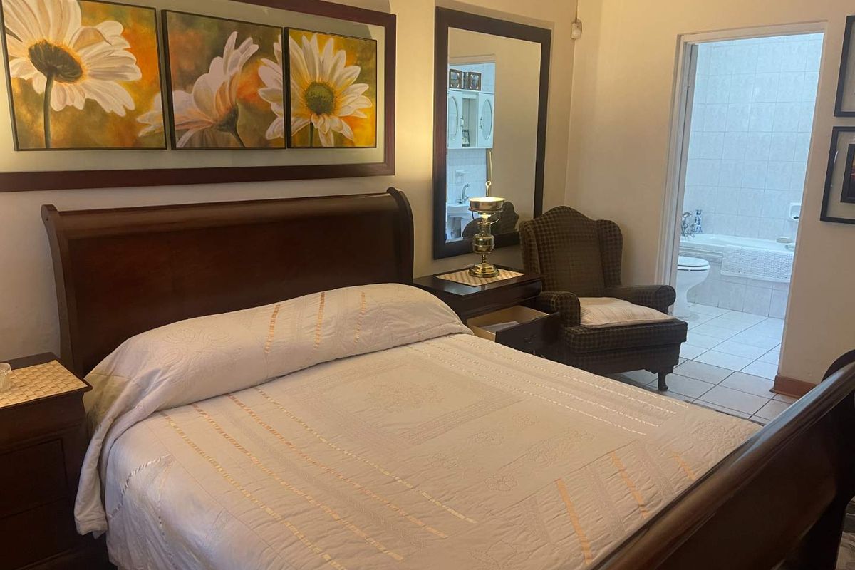 A well-maintained bedroom featuring neutral walls and an en-suite bathroom with tiled flooring and a bathtub.
