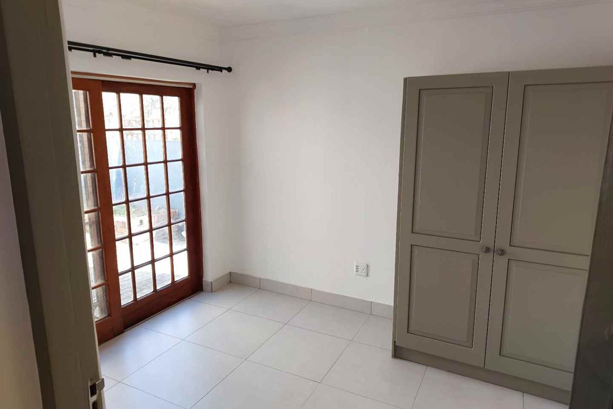 A bright bedroom featuring neutral floor tiles, a built-in wardrobe, and a wooden framed glass door providing access to the exterior.