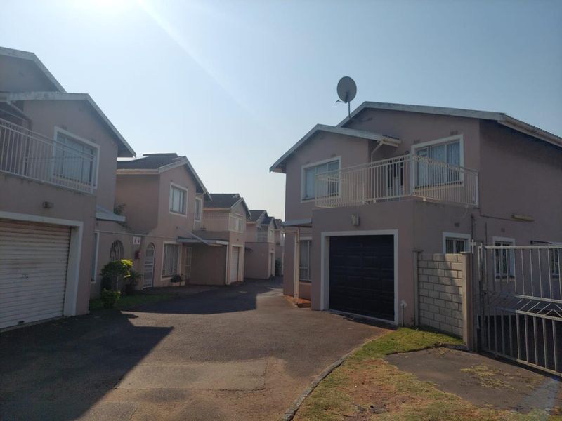 Exterior view of a townhouse complex featuring multiple units with garages, balconies, and a shared asphalt driveway.