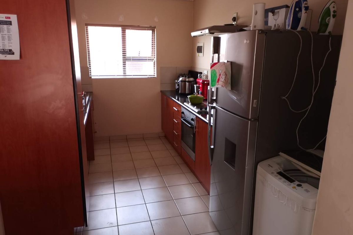 Functional kitchen featuring wooden cabinetry, tiled flooring, built-in oven, and hob, providing a practical workspace with natural light from the window.
