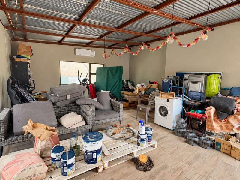 A covered patio area featuring tiled flooring, exposed timber rafters, and a corrugated metal roof, currently utilized as a multi-purpose storage and utility space.