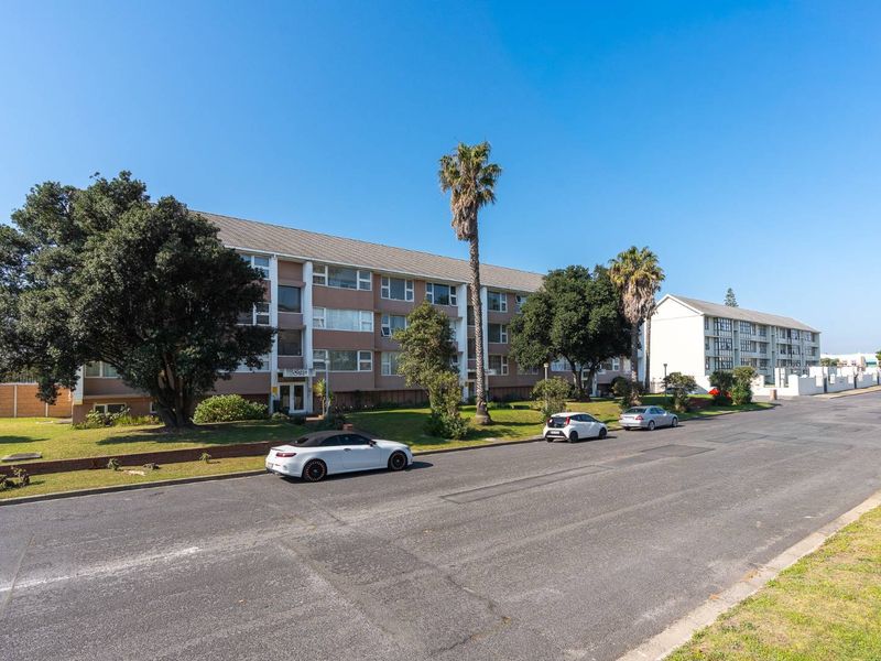Street-level view of a multi-story apartment complex featuring a landscaped front lawn and paved access.