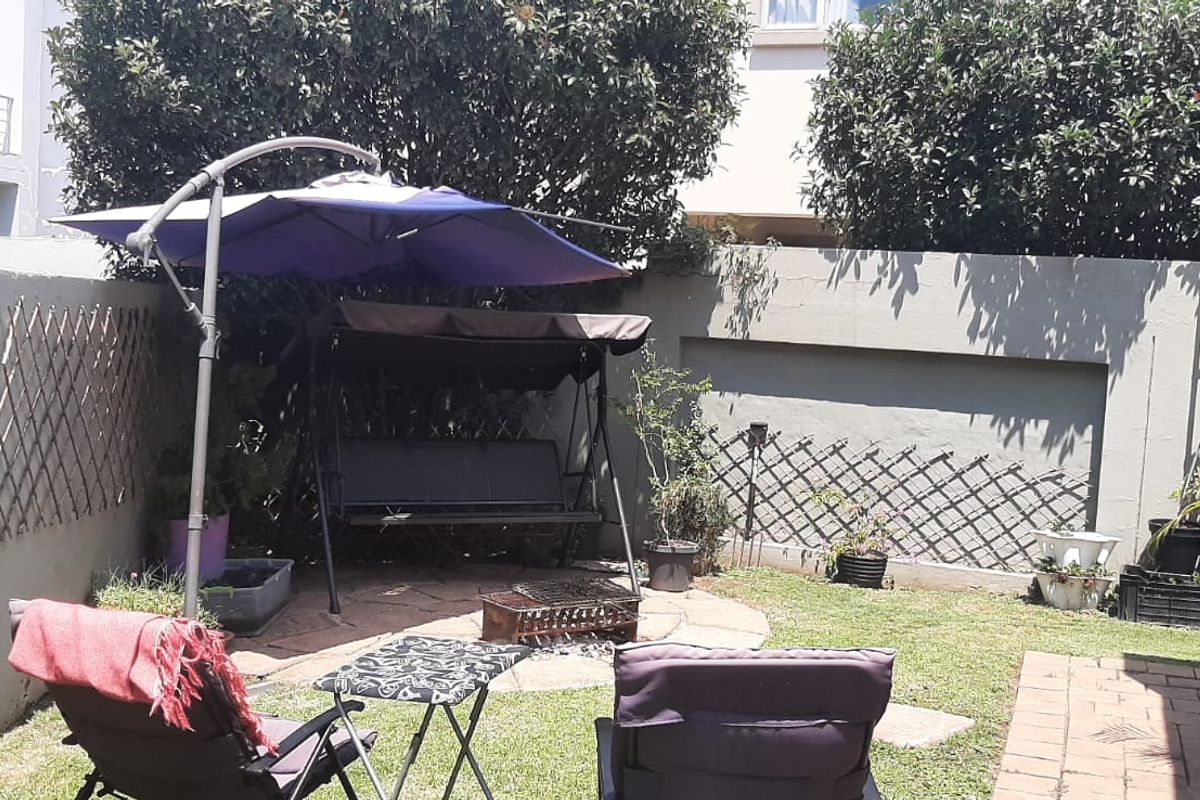 A private rear garden area featuring a paved section, lawn, and high boundary walls for added privacy.