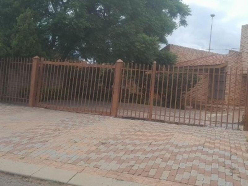 Front view of a residential property featuring a face brick facade, tiled roof, and a secure metal perimeter fence with paved driveway.