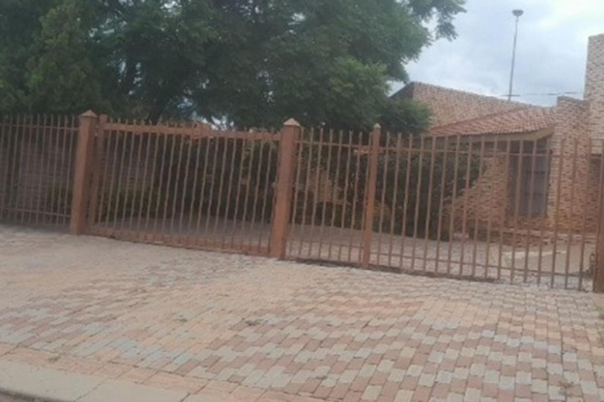 Front view of a residential property featuring a face brick facade, tiled roof, and a secure metal perimeter fence with paved driveway.