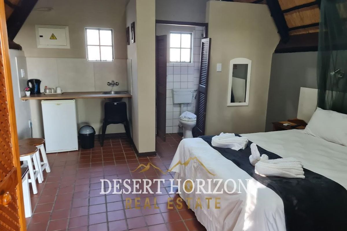 A hotel bedroom featuring a kitchenette area with a sink and counter, adjacent to an en-suite bathroom with tiled flooring and thatched roof detail.