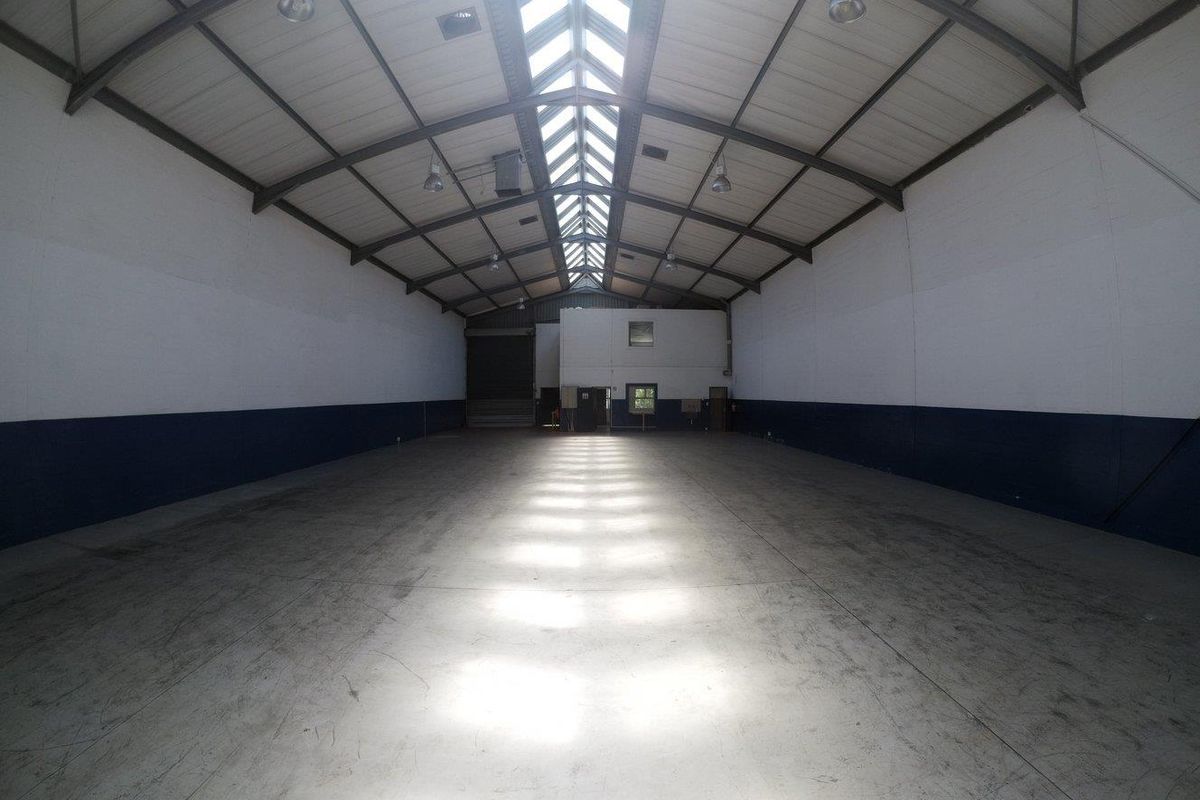 Spacious industrial warehouse unit featuring high ceilings with skylights, exposed steel trusses, durable concrete flooring, and an integrated mezzanine office area.