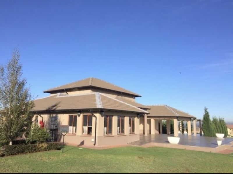 Rear view of the property featuring a tiled roof, expansive paved patio area, and well-maintained surrounding lawn.