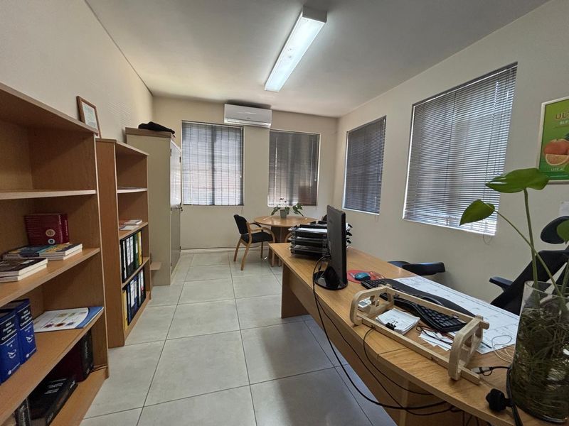 A functional office space featuring tiled flooring, air conditioning, and multiple windows with venetian blinds, providing a bright and practical work environment.