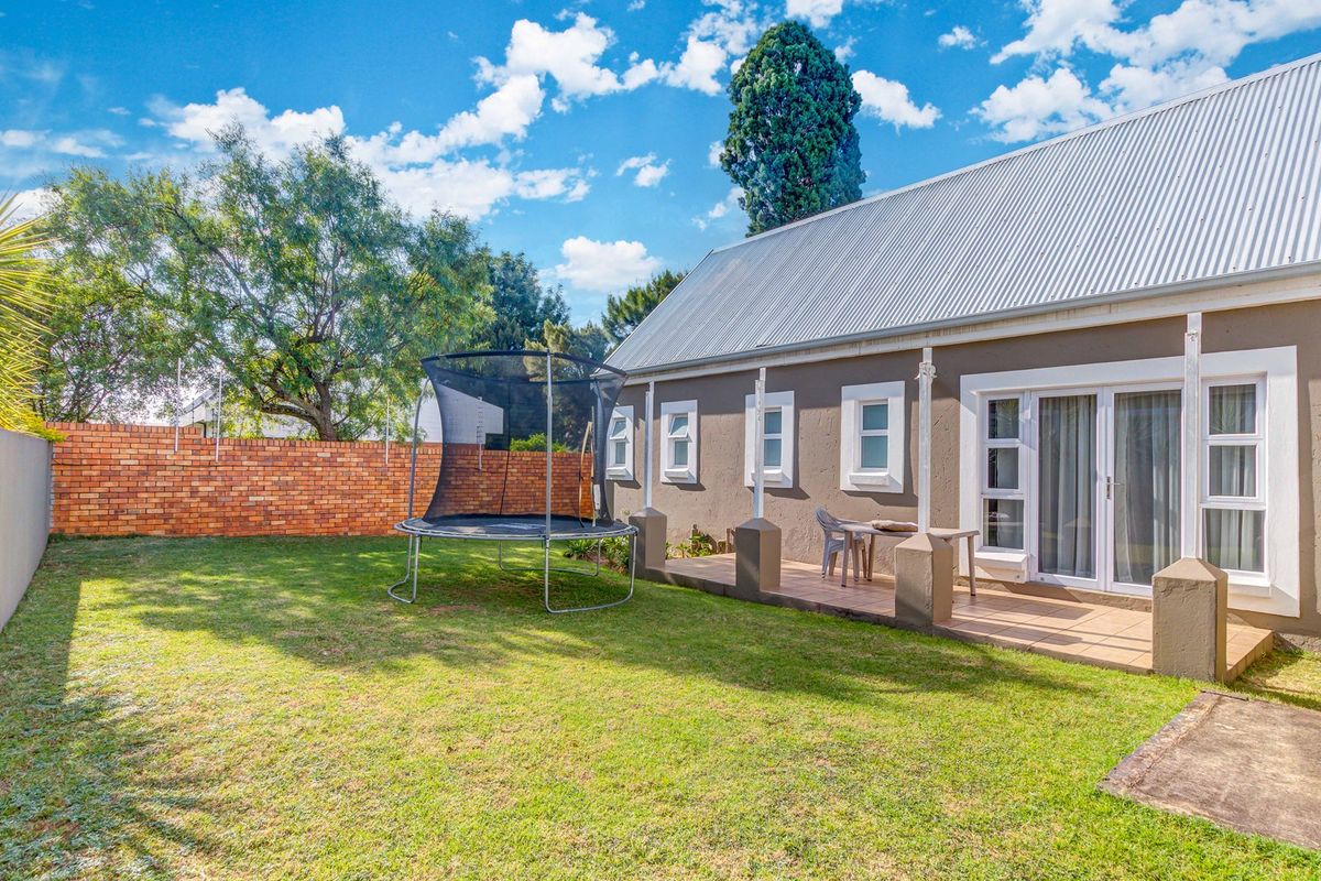 Rear view of the property featuring a tiled patio, sliding glass doors, and a private garden enclosed by a brick boundary wall.