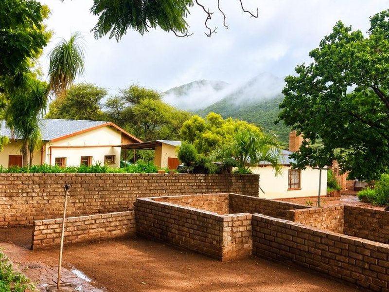 A rear garden area featuring rustic brick walls, paved pathways, and views of the surrounding mountain landscape.