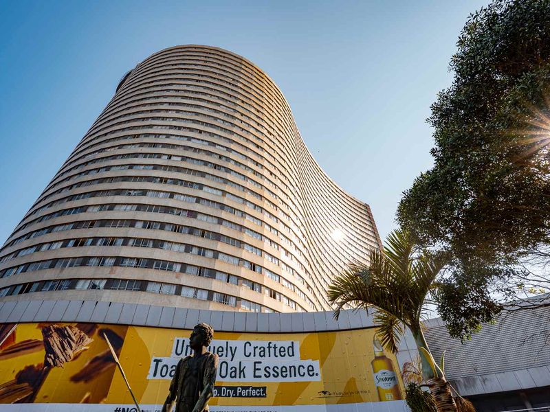 A low-angle exterior view of a large, curved high-rise apartment building featuring a prominent ground-level advertisement.