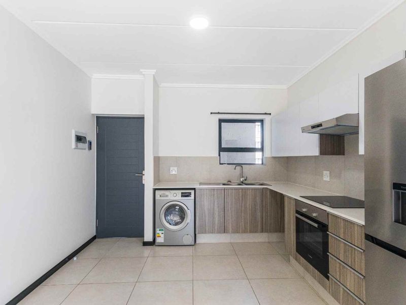 Modern kitchen featuring sleek wood-grain cabinetry, stone countertops, integrated oven and hob, and tiled flooring in a clean, contemporary apartment setting.
