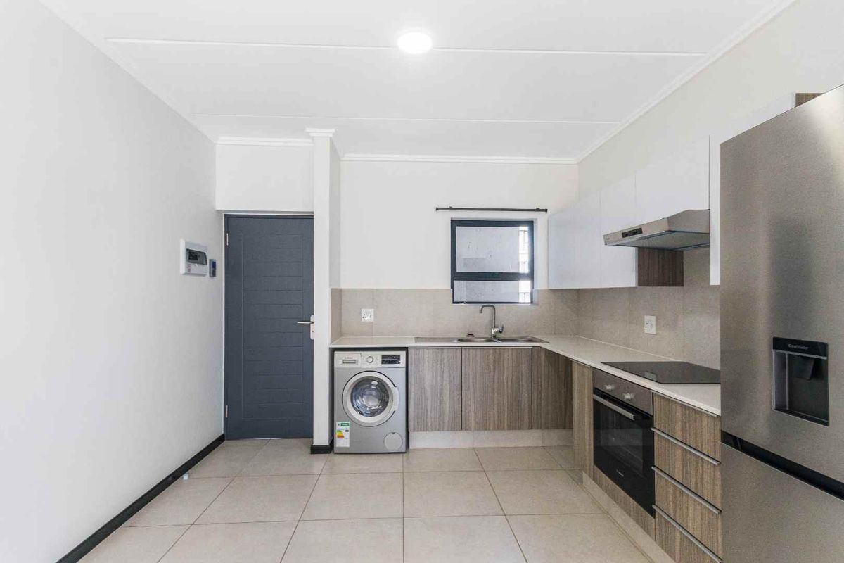 Modern kitchen featuring sleek wood-grain cabinetry, stone countertops, integrated oven and hob, and tiled flooring in a clean, contemporary apartment setting.