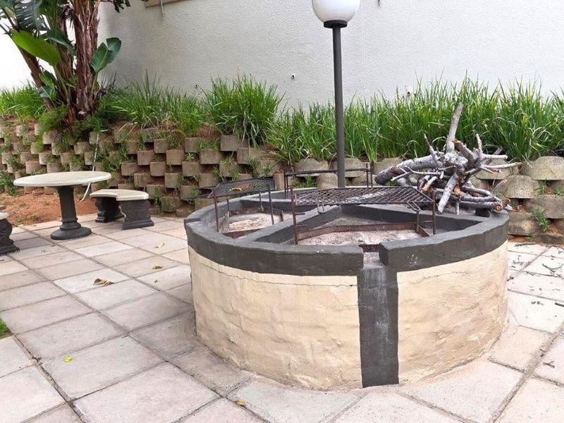 Outdoor entertainment area featuring a circular built-in braai, paved patio, and tiered retaining wall with garden landscaping.